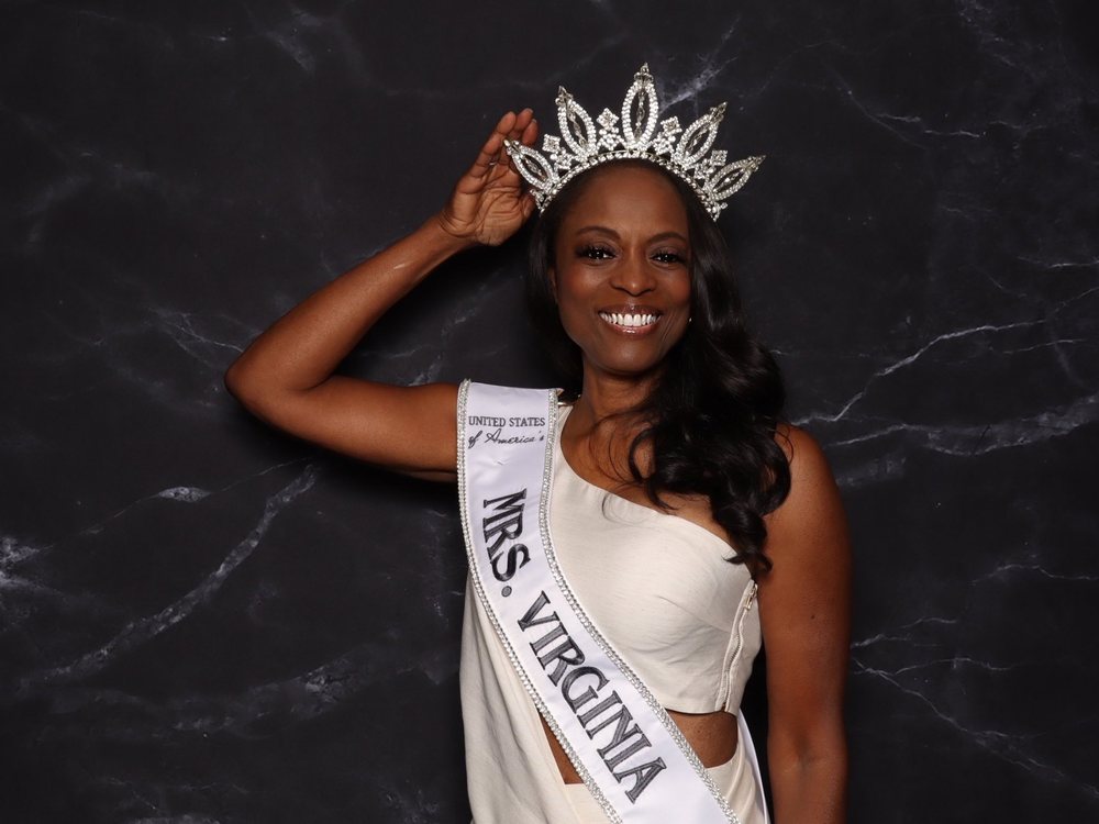 Mrs. Virginia in her crown and sash smiling at the black marble backdrop photo booth at a bridal expo in Chesapeake