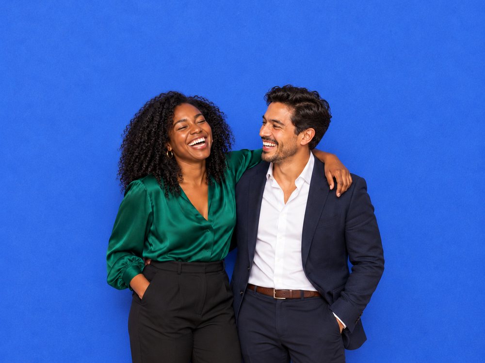 Two coworkers laughing in front of a solid blue photo booth backdrop at a corporate event in Norfolk
