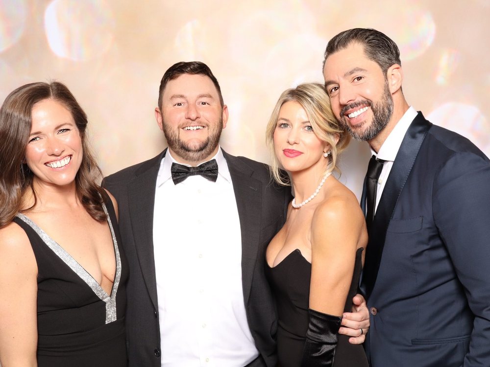 Two couples in black tie posing at the champagne sparkle backdrop at the VBSPCA Wags and Whiskers Gala in Virginia Beach