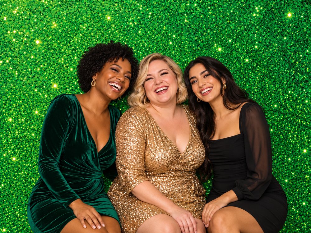 Three friends in velvet and gold sequins laughing at an emerald green sparkle backdrop photo booth at a holiday party in Richmond