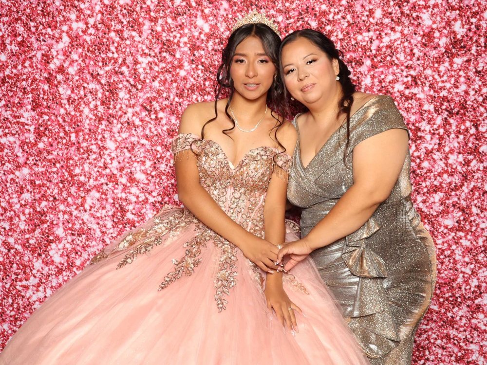 A quinceañera in a pink ball gown cheek to cheek with her mom at a rose gold glitter photo booth in Perth Amboy