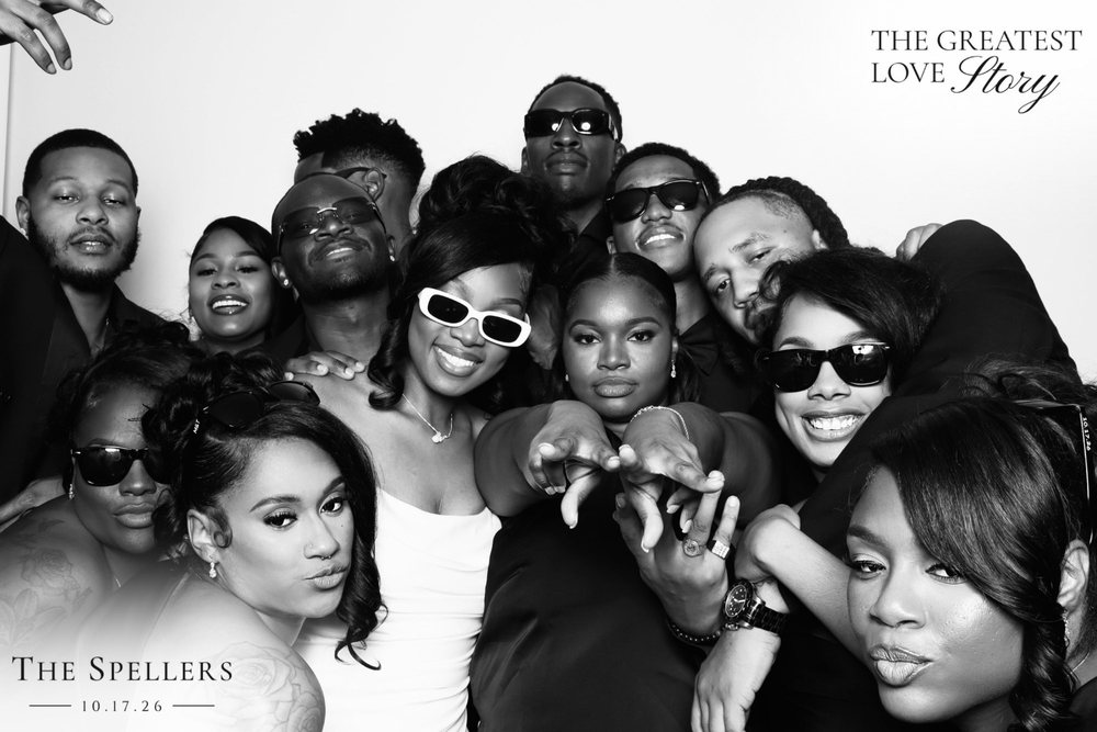 Makima in white sunglasses surrounded by a crowd of friends at a black-and-white wedding photo booth at the Signet Center in Chesapeake