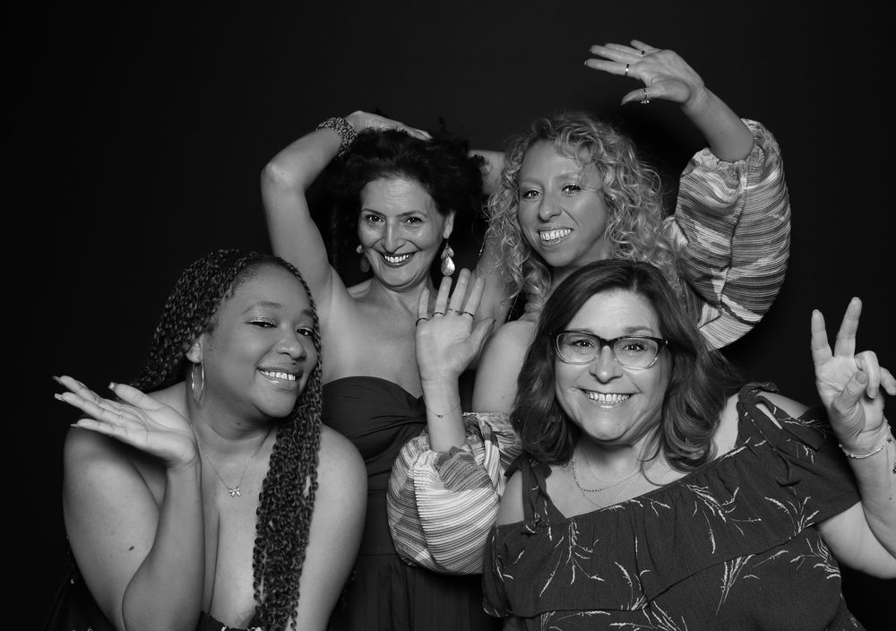 Four friends laughing and posing at a black-and-white party photo booth in Virginia Beach