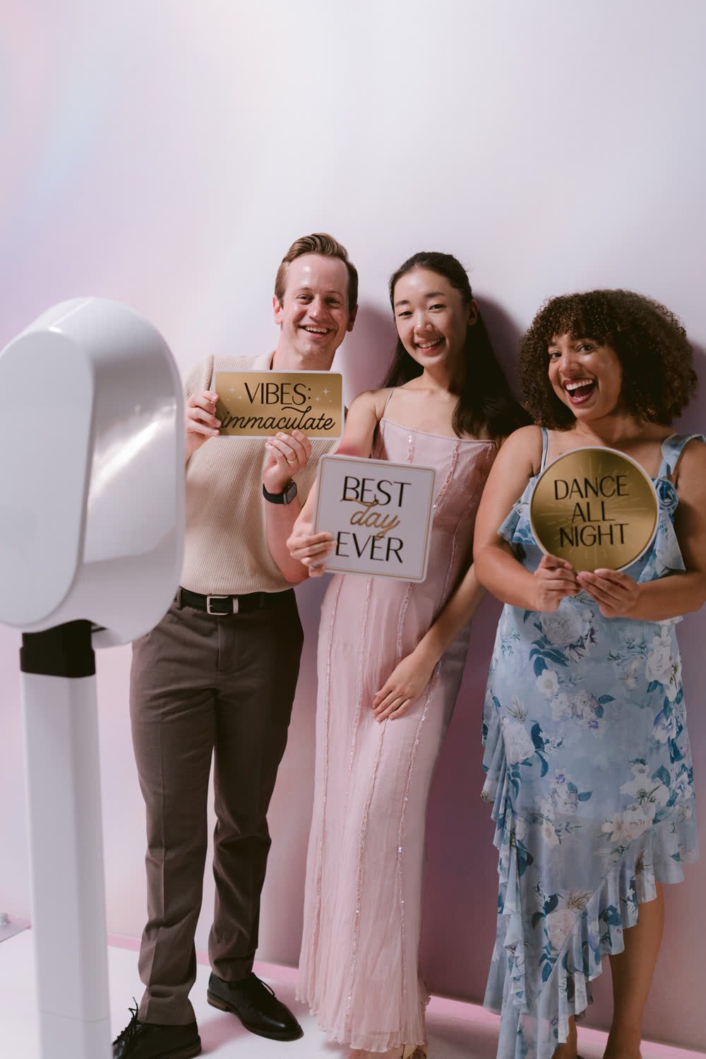 Three friends holding Vibes Immaculate, Best Day Ever, and Dance All Night signs at the self-serve photo booth