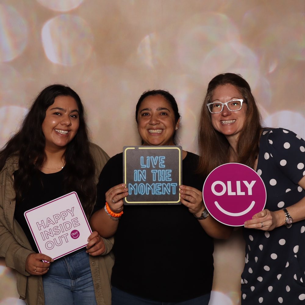 Three coworkers holding branded signs at a corporate offsite photo booth in San Francisco