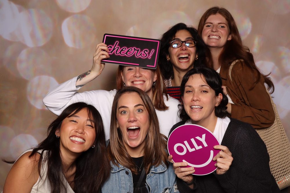 A team holding OLLY and cheers signs at a corporate offsite photo booth in San Francisco