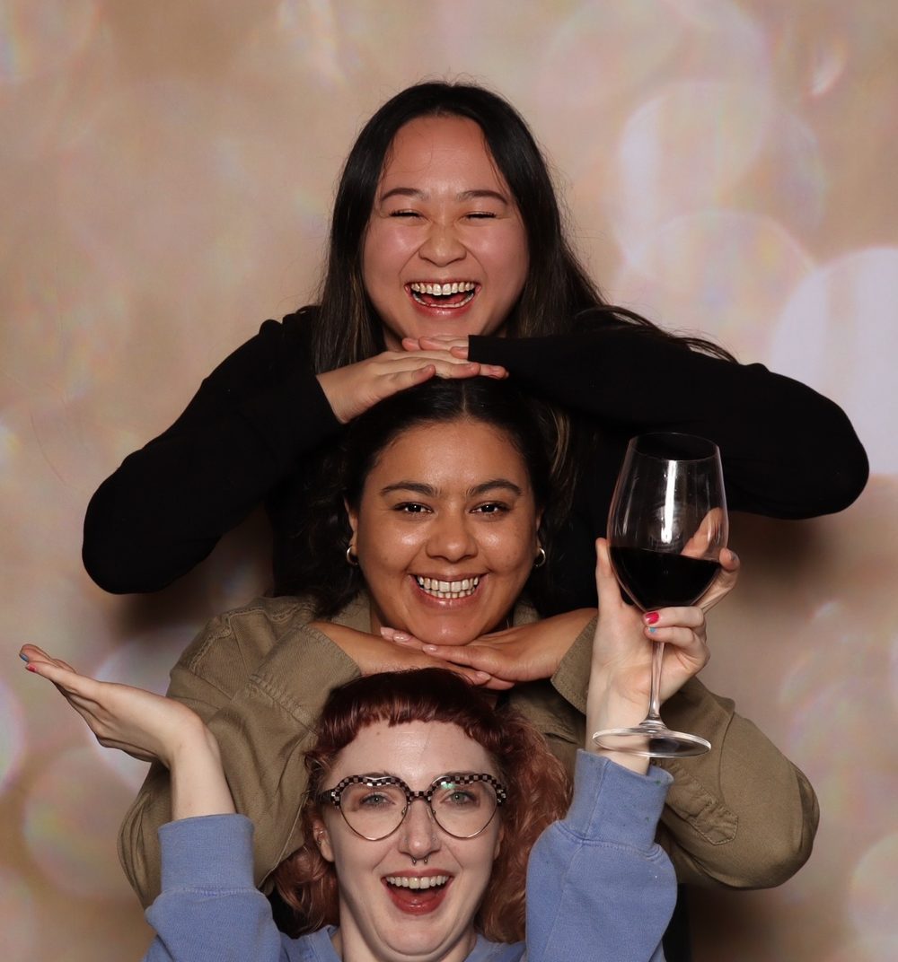 Three coworkers stacked playfully at a corporate event photo booth in San Francisco