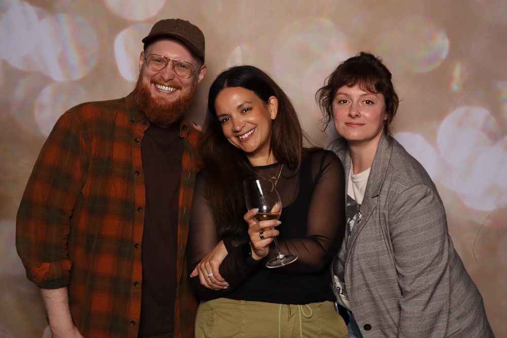 Three coworkers posing with drinks at a corporate offsite photo booth in San Francisco