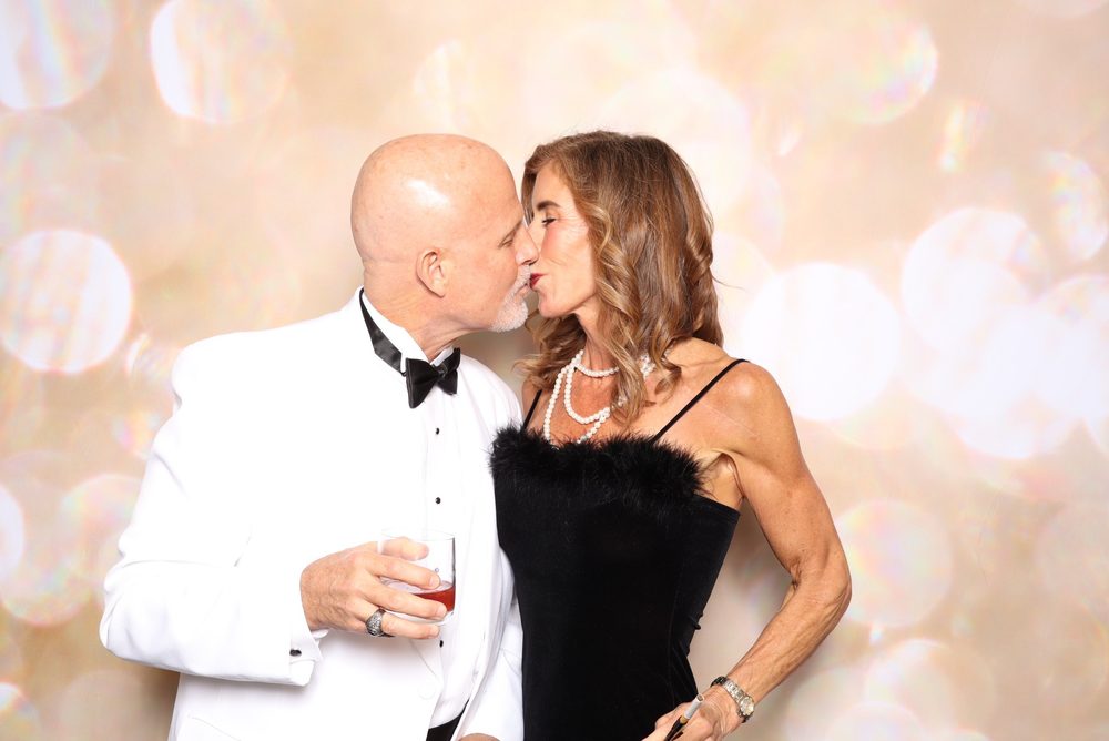 A couple sharing a kiss at a black-tie gala photo booth in Virginia Beach
