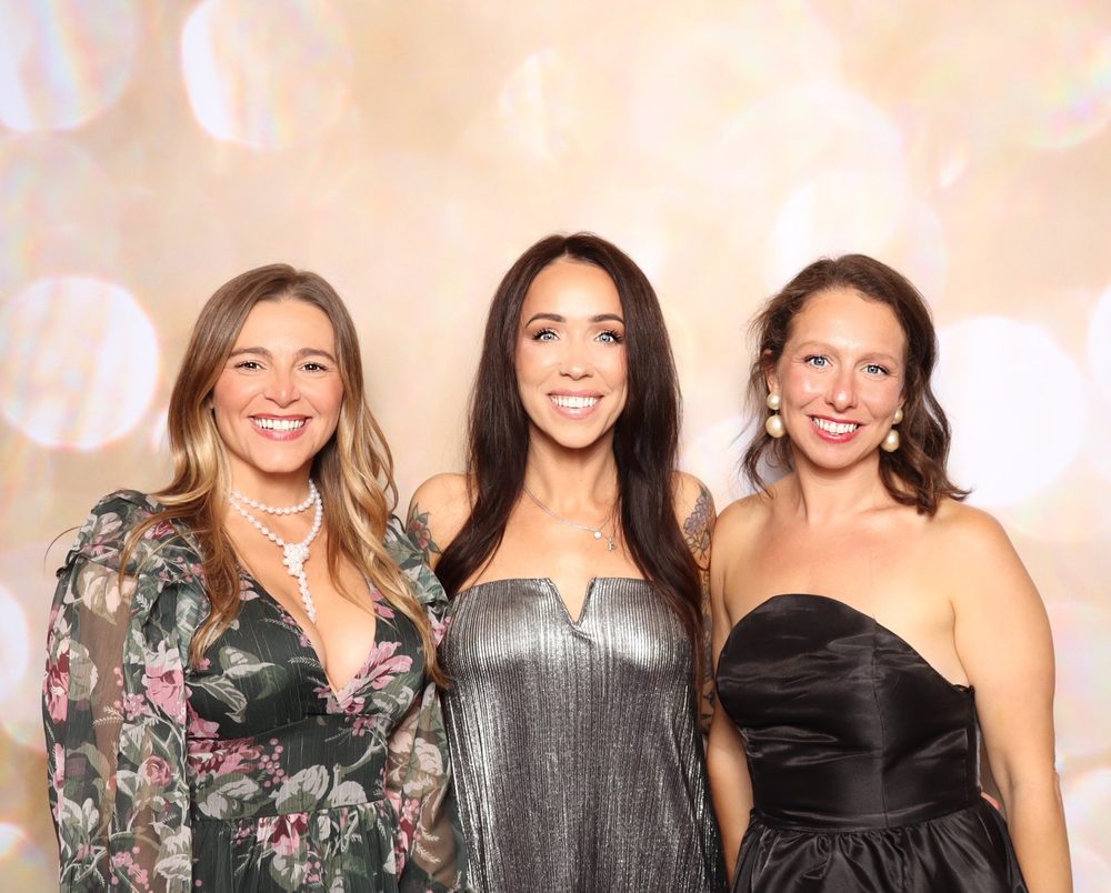 Three women in gowns smiling at the Wags and Whiskers Gala photo booth in Virginia Beach