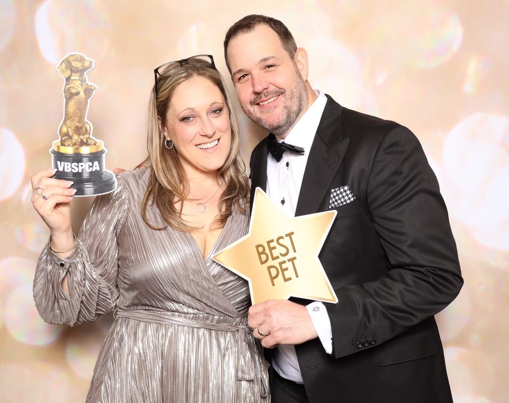 A couple holding a trophy and Best Pet sign at a charity gala photo booth in Virginia Beach