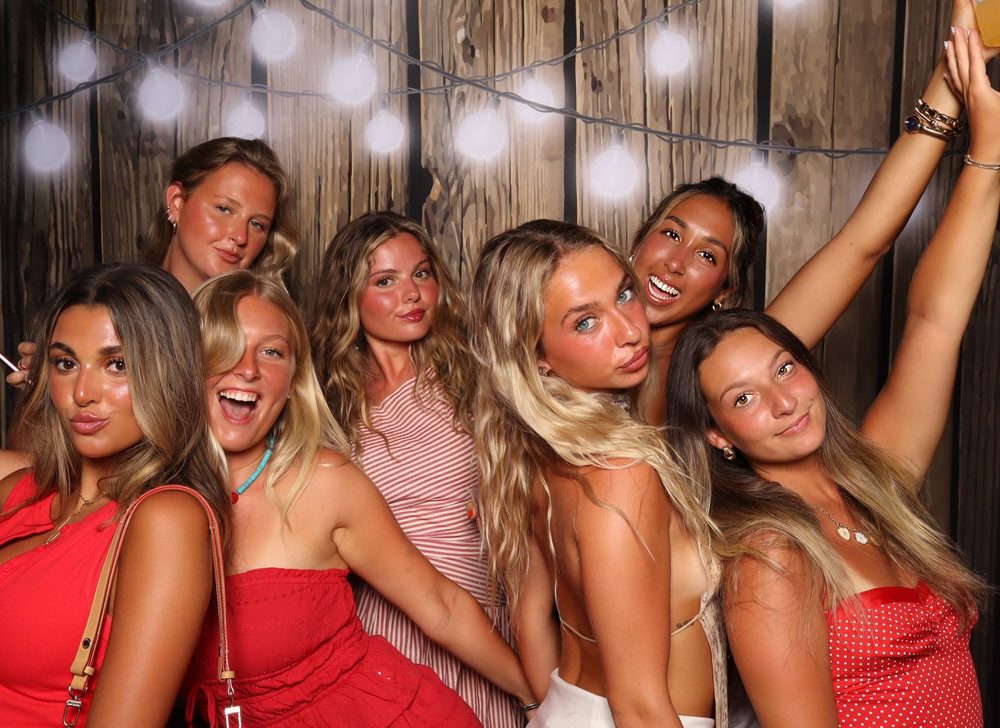 Friends throwing their arms up under string lights at a birthday party photo booth in Virginia Beach
