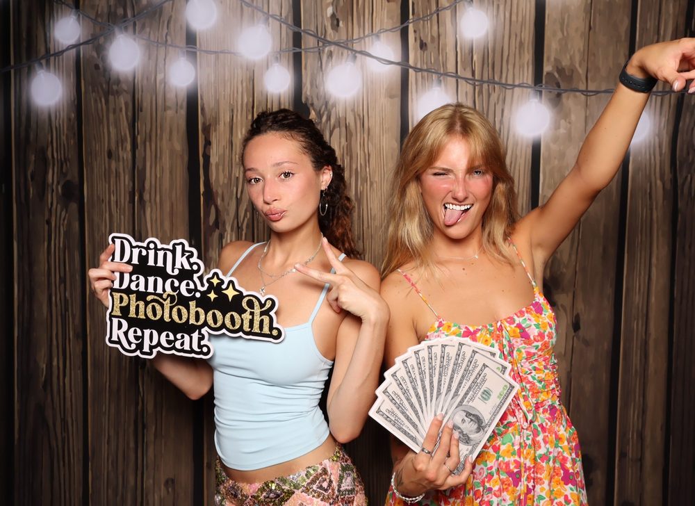 Two friends with props and arms up at a Virginia Beach Independence Day party photo booth