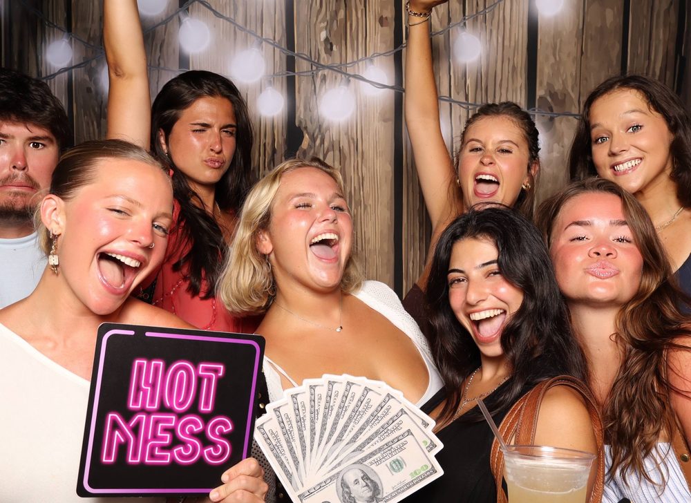 A crowd of friends screaming with a Hot Mess sign at a Virginia Beach party photo booth