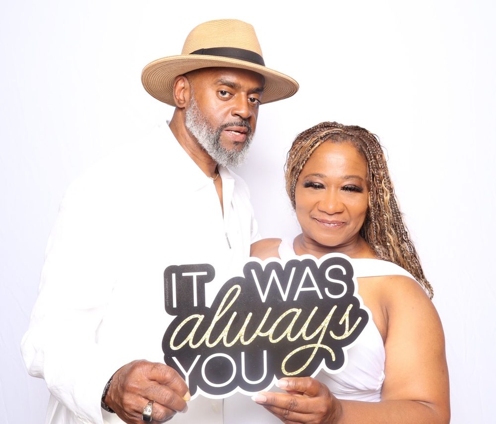 A couple holding an It Was Always You sign at an all-white party photo booth in Virginia Beach