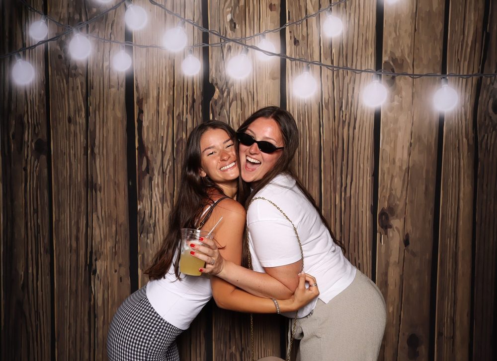 Two friends in a laughing hug at a Virginia Beach Independence Day party photo booth