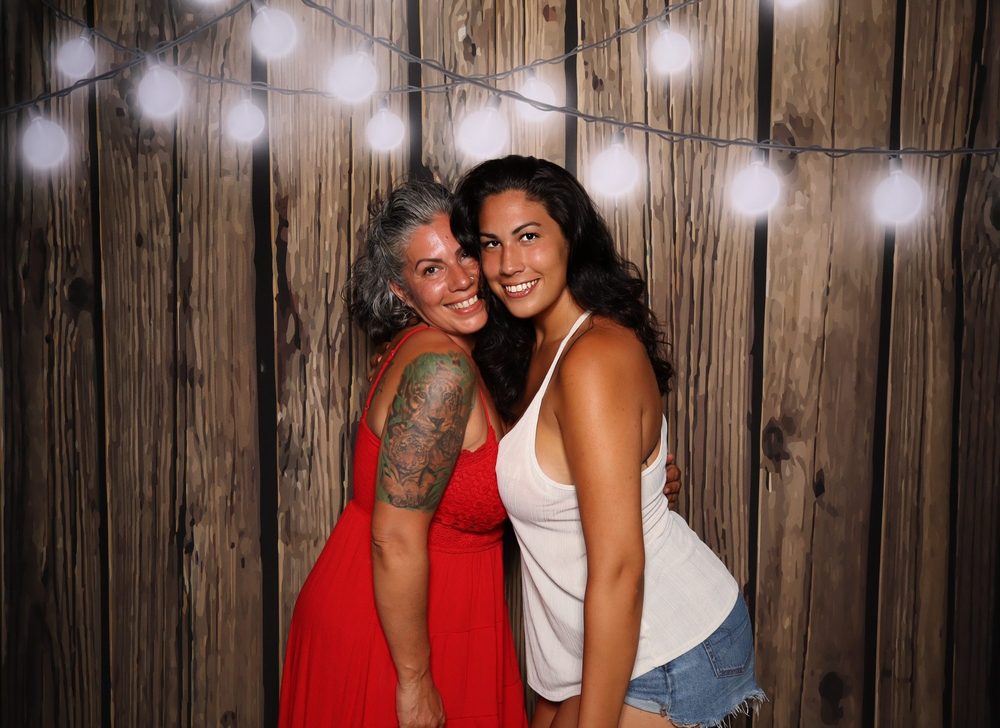 Two friends smiling cheek to cheek at a summer party photo booth in Virginia Beach