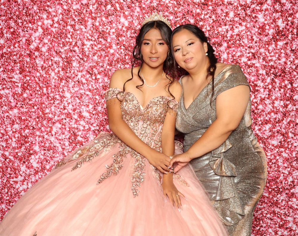 A quinceañera and her mom cheek to cheek at a rose gold glitter photo booth in Perth Amboy, New Jersey