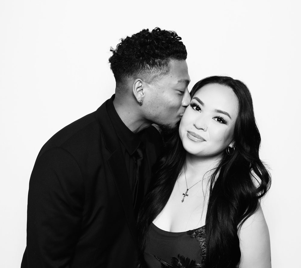 Wedding guests sharing a cheek kiss at a black-and-white photo booth in Virginia Beach