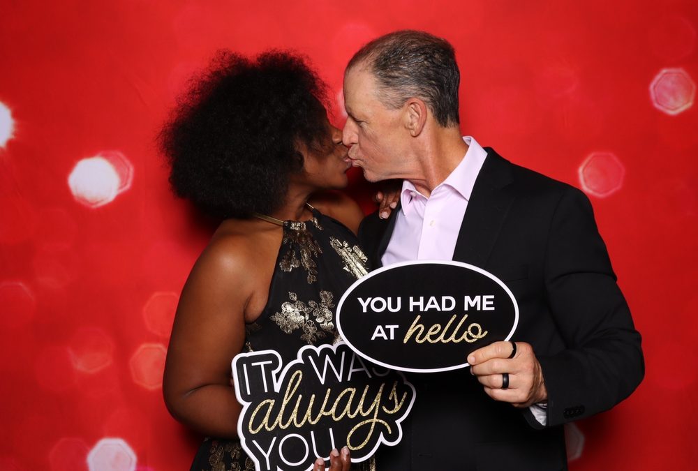 A guest couple kissing with sign props at a Suffolk wedding photo booth