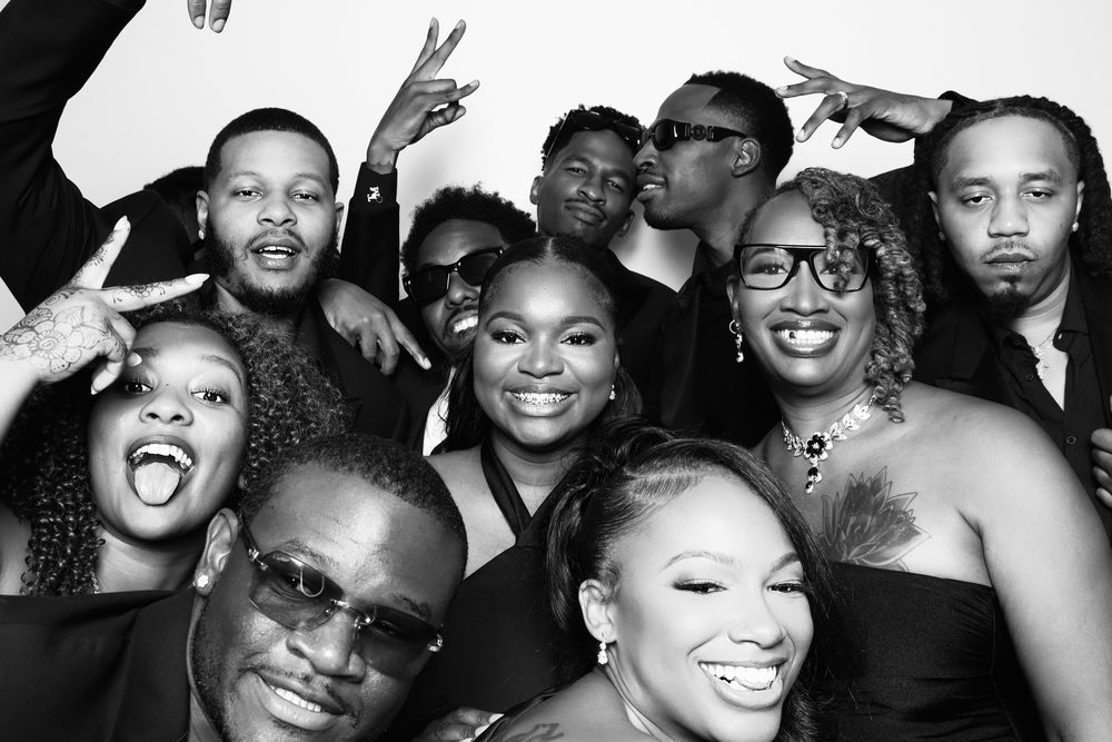 A packed crowd of wedding guests laughing at a black-and-white photo booth in Chesapeake