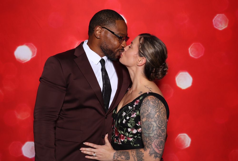 A guest couple sharing a kiss at a red-backdrop wedding photo booth in Suffolk