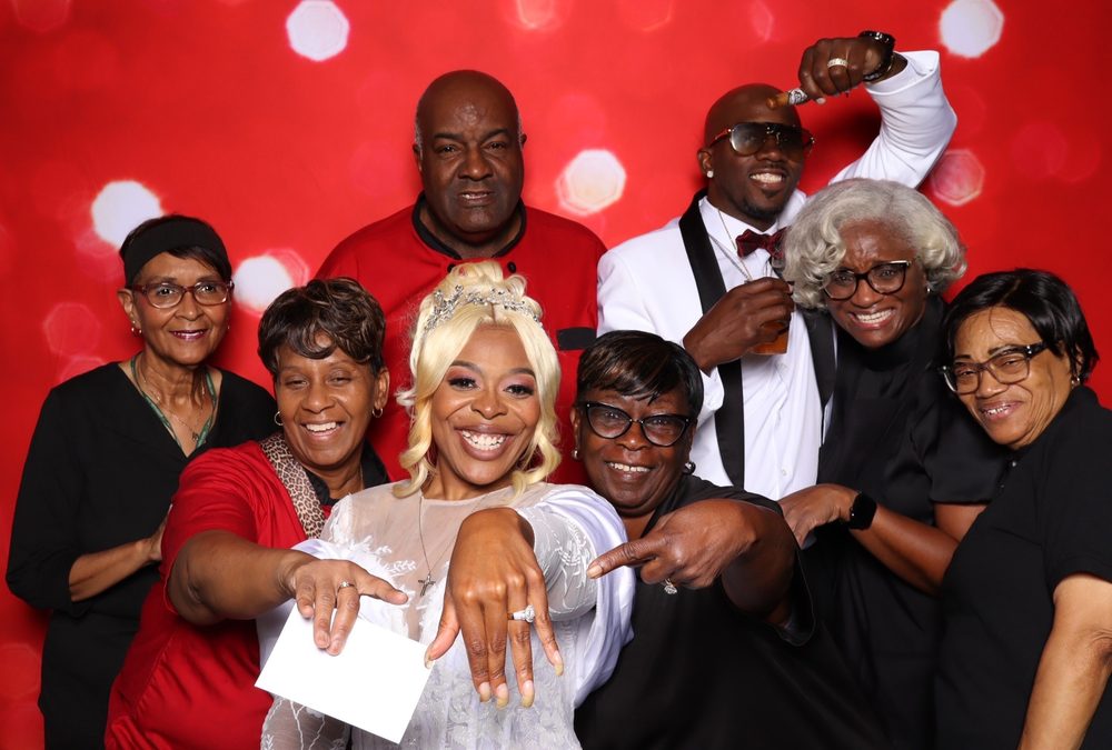 A bride showing off her ring surrounded by family at a Suffolk wedding photo booth