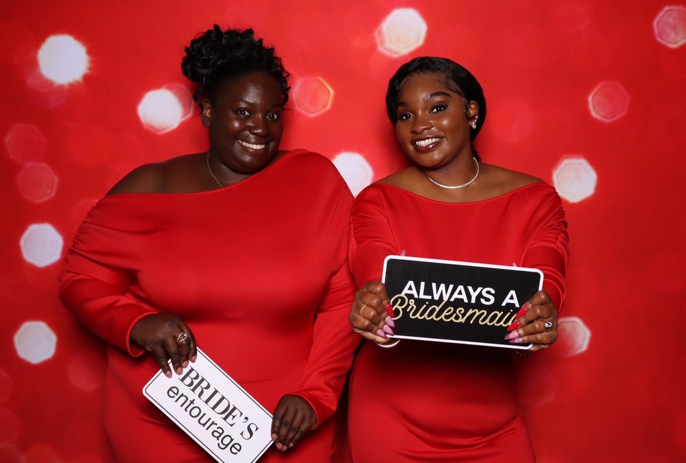 Two bridesmaids with an Always a Bridesmaid sign at a wedding photo booth in Suffolk