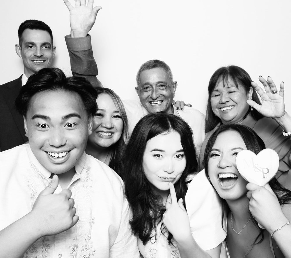 A bride and groom crowded in with family at a black-and-white wedding photo booth in Virginia Beach