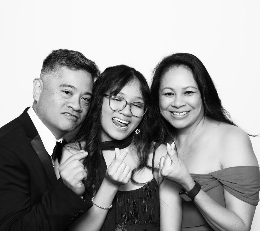 A family of three smiling together at a black-and-white wedding photo booth in Virginia Beach
