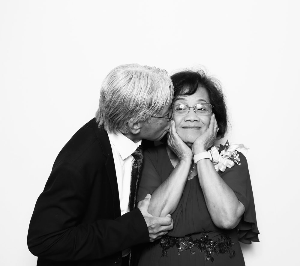 An older guest kissing his wife on the cheek at a wedding photo booth in Virginia Beach