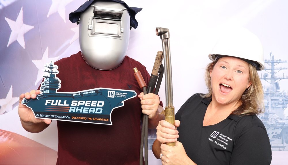 A guest in a welding helmet and a Newport News Shipbuilding recruiter with a cutting torch at the Cook Out 400 photo booth at Richmond Raceway in Richmond
